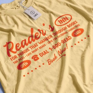 May include: A yellow t-shirt with a red graphic that says "Reader's Inn" and includes the text "For minds that wander through books, TBR piles, late night reads, love for fictional characters, Dial 1-800-READ, Daily, Book Now!"