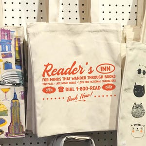 May include: White canvas tote bag with red text that reads "Reader's Inn" and "For minds that wander through books."  The bag also has a red phone icon and the text "Dial 1-800-READ".