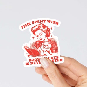 May include: Red and white sticker with a retro illustration of a woman reading a book with a cat in her lap. The text reads "Time spent with books and cats is never wasted."