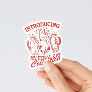 Puede incluir: Una pegatina blanca con texto rojo e ilustraciones de tres gatos bailando. El texto dice "Introducing My Feral Cat Collection."