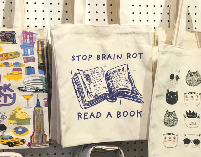 May include: A white tote bag with a blue and white illustration of an open book and the text "STOP BRAIN ROT READ A BOOK".