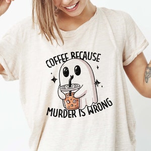 May include: Beige t-shirt with the text "COFFEE BECAUSE MURDER IS WRONG." The graphic features a cartoon ghost holding an iced coffee. The ghost is white with black eyes and a black straw.