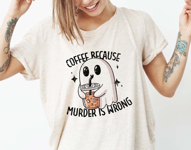 May include: Beige t-shirt with the text "COFFEE BECAUSE MURDER IS WRONG." The graphic features a cartoon ghost holding an iced coffee. The ghost is white with black eyes and a black straw.