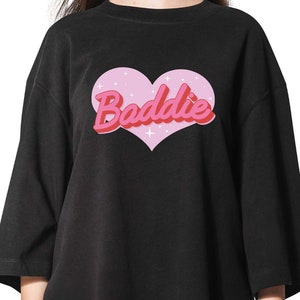 May include: Black oversized t-shirt with a pink heart graphic and the text "Baddie" in pink and red letters.