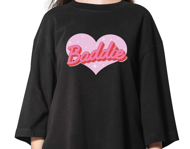 May include: Black oversized t-shirt with a pink heart graphic and the text "Baddie" in pink and red letters.