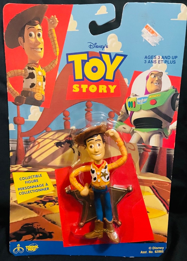 K&ouml;nnte beinhalten: Sammelfigur von Woody aus Toy Story, eine Cowboy-Puppe mit braunem Hut, gelbem Hemd, blauer Jeans und rotem Halstuch. Die Figur steht auf einem sternf&ouml;rmigen Sockel. Die Verpackung ist rot und blau mit dem Toy Story-Logo und dem Text "Ages 3 and Up".