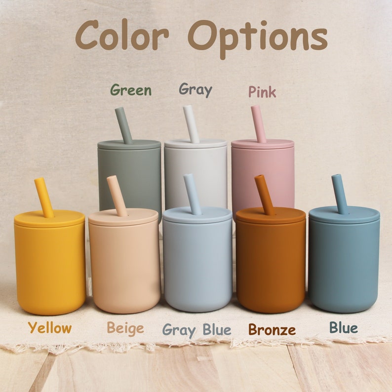 Eight personalized silicone baby sippy cups with different colors on the wooden table. Their colors are as follows: green; gray; pink; yellow; beige; gray blue; bronze; blue.
