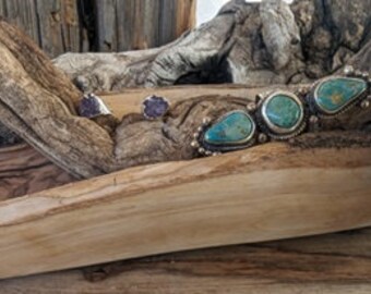 May include: A pair of silver earrings with purple stones and a turquoise and silver bracelet with three turquoise stones.