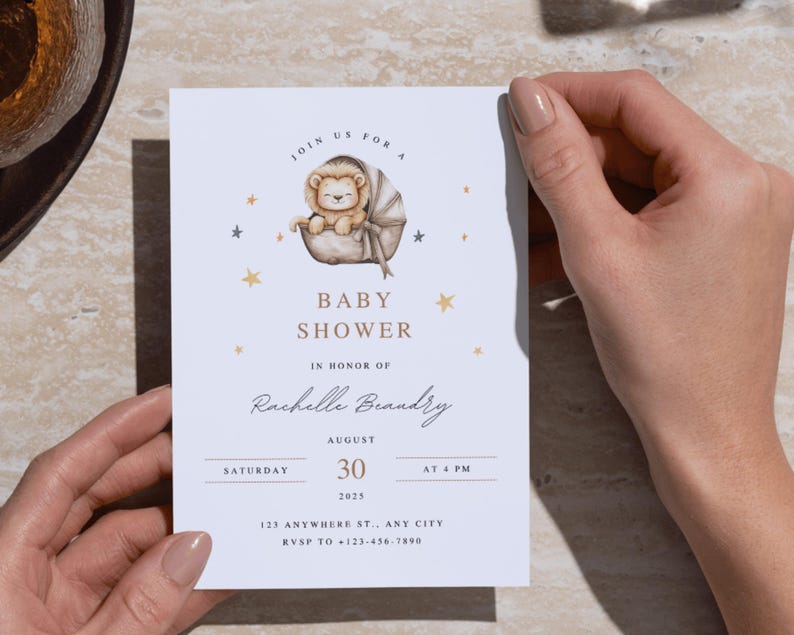 May include: Baby shower invitation featuring a watercolor illustration of a lion cub in a bassinet, surrounded by gold stars. The invitation includes the text "Baby Shower" and event details for Rachelle Brandry, August 30, 2025, at 4 PM.