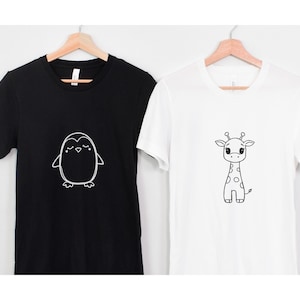 May include: Two t-shirts, one black and one white, each with a simple cartoon animal design. The black shirt features a penguin, and the white shirt has a giraffe. Both designs are in black and white.