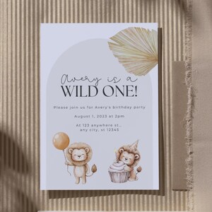 May include: A birthday party invitation with the text "Avery is a WILD ONE!". The invitation features illustrations of a lion holding a balloon and a lion with a cupcake. The invitation is on a white background with a beige arch and a dried palm leaf.
