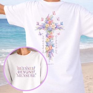 Puede incluir: Camiseta blanca con un diseño de cruz floral. La cruz está adornada con flores rosas, moradas y amarillas, y mariposas. El texto "Give thanks to the Lord" está impreso verticalmente en el lado derecho de la cruz. El texto "Psalm 107:1" está impreso debajo.