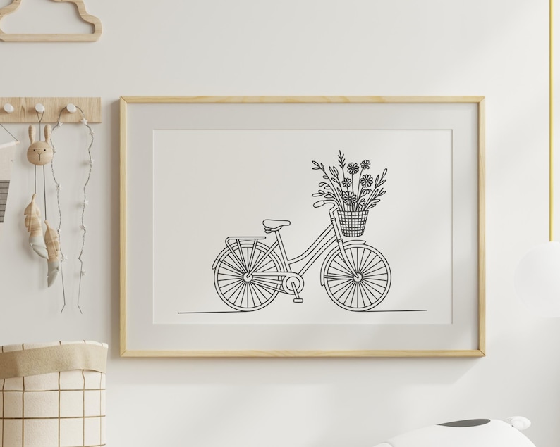 May include: A framed black and white line drawing of a bicycle with a basket of flowers. The bicycle has a classic design with a rear rack and is set against a white background. The frame is a light wood color.