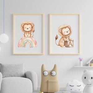 May include: Two framed watercolor prints featuring a lion cub. One sits atop a rainbow, the other with a block displaying the letter "A". The prints have light wood frames and are displayed in a nursery setting.