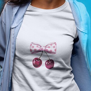 May include: White t-shirt with a pink and white polka dot bow and two pink cherries.