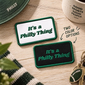 May include: Two rectangular embroidered patches with green borders and the text It's a Philly Thing. One patch has a white background with dark green text, and the other has a black background with green text. The text Two color options is visible.