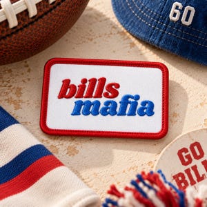 May include: A rectangular embroidered patch with a white background and a red border. The text bills is stitched in red, and the text mafia is stitched in blue. The patch is positioned among various sports-themed items including a football.