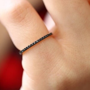 Puede incluir: Un fino anillo de oro con una fila de pequeños diamantes negros.