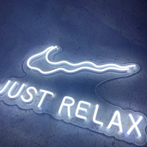 Puede incluir: Un letrero de neón blanco con las palabras "JUST RELAX" y una línea ondulada sobre el texto.
