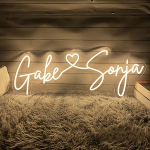Può includere: Segno al neon bianco con i nomi "Jake" e "Sonja" collegati da un simbolo di cuore.