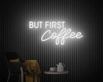 May include: White neon sign with the text "But First Coffee" on a black wall with a black chair and a small table with a coffee cup and a teapot.