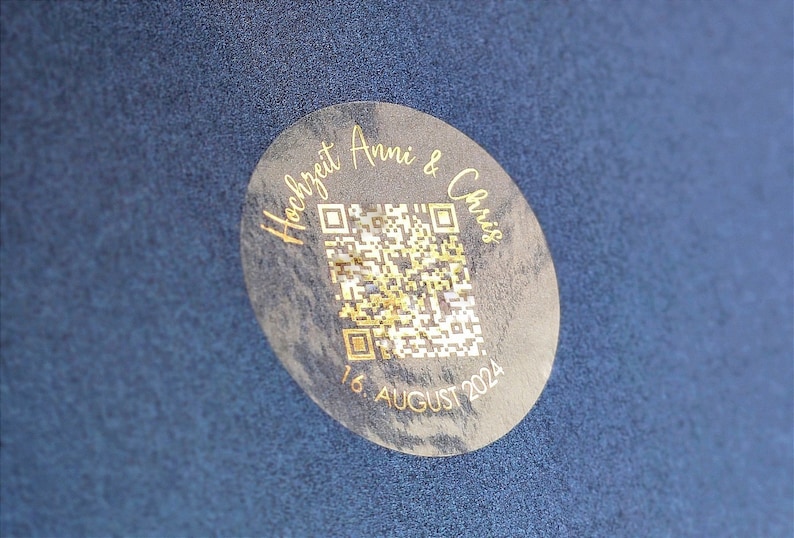 May include: A round, clear sticker with a gold design. The sticker says "Hochzeit Anni & Chris" and "16. AUGUST 2024" and features a QR code.