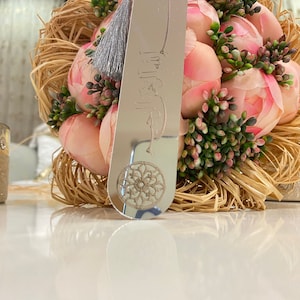 May include: A silver bookmark with a tassel and an engraved design. The bookmark is resting on a bouquet of pink flowers.
