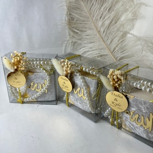 May include: Three clear boxes with white velvet fabric inside. Each box has a gold circle with the text "Dalia & Kyle May 4, 2024" and a string of white pearls.