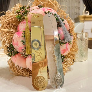 May include: Two gold and silver bookmarks with tassels. The bookmarks feature Arabic calligraphy and a decorative design.