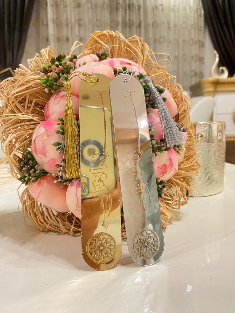 May include: Two gold and silver bookmarks with tassels. The bookmarks feature Arabic calligraphy and a decorative design.