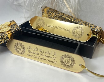 Peut inclure: Deux marque-pages dorés avec un motif décoratif et du texte arabe. Le marque-page de gauche porte le texte "أقْرَأْ بِاسْمِ رَبِّكَ الَّذِي خَلَقَ Recite in the name of your Lord who created" et le marque-page de droite porte le texte "Omar Al Hallak".