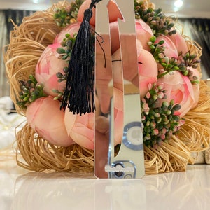 May include: A silver bookmark with a black tassel. The bookmark is shaped like an arrow and has a reflective surface.