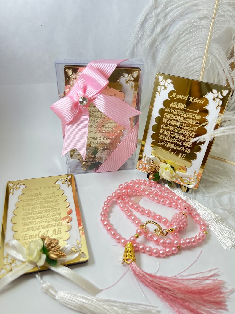 May include: A pink and gold Islamic prayer set with a small framed verse, a larger framed verse, and a pink prayer bead necklace with a tassel.