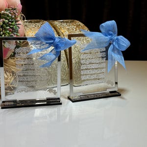 May include: Two clear glass frames with engraved text and blue bows. The frames are on a white surface. The text on the frames reads "Welcome Baby A" and "Welcome Baby Z".