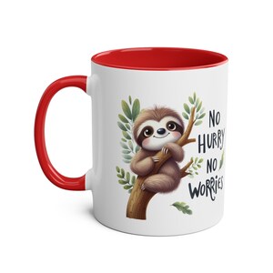 Könnte beinhalten: Eine weiße Keramiktasse mit rotem Rand. Die Tasse zeigt ein Cartoon-Faultier, das an einem Ast mit grünen Blättern hängt. Der Text "No hurry no worries" ist auf die Tasse gedruckt.