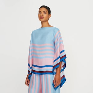 Puede incluir: Una blusa de rayas azules y rosas con una silueta amplia y fluida. La blusa tiene un cuello barco y un ajuste holgado. Las mangas son de tres cuartos y tienen una forma amplia y fluida. La blusa está hecha de una tela suave y sedosa.