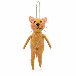May include: A felted wool cat ornament in a golden-brown hue, featuring pink-tinted cheeks, black bead eyes, a dark triangular nose, and thin black whiskers. The cat has a simple upright posture with a jute string loop attached to the top.