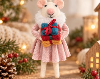 May include: A felt mouse ornament with a pink nose and ears, wearing a textured pink dress with a white faux fur collar. The mouse holds a stack of three small wrapped gifts in teal, red, and yellow, tied together with a thin red ribbon.