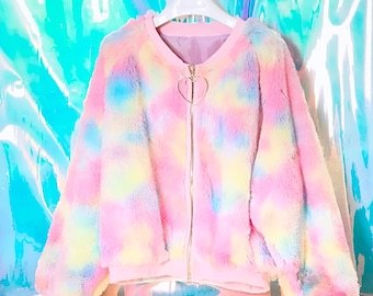 Puede incluir: Una chaqueta de piel sintética de manga larga con un patrón tie-dye en tonos pastel de rosa, azul y amarillo. La chaqueta tiene cuello redondo, puños acanalados, dobladillo acanalado y un cierre de cremallera dorado con un tirador en forma de corazón.