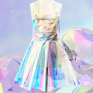 May include: An iridescent, transparent, halter-style overall dress with a skirt that flares out. The dress is made of a shiny, reflective material that creates a rainbow effect.