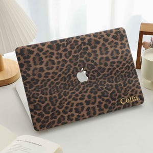 May include: A laptop skin featuring a brown and black leopard print pattern with the name Colin. printed in gold lettering in the bottom right corner. The skin is applied to the lid of a laptop, displaying the silver Apple logo in the centre.