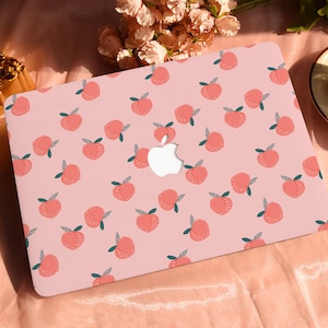 Puede incluir: Una piel de portátil rosa con un patrón repetido de fruta de melocotón. La piel tiene un recorte para el logotipo de Apple.