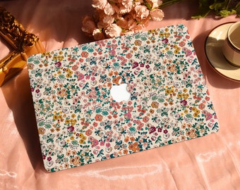 May include: A white laptop with a floral pattern on the lid. The pattern features small pink, yellow, and blue flowers on a white background. The Apple logo is visible on the lid.