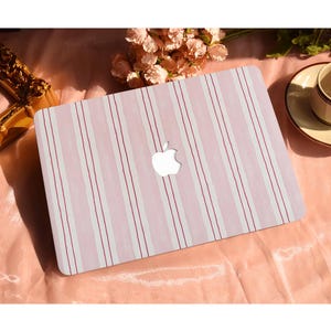 May include: A laptop featuring a pink and white striped pattern. The design has vertical stripes, with thin red lines separating the wider white and pink stripes. The Apple logo is visible.