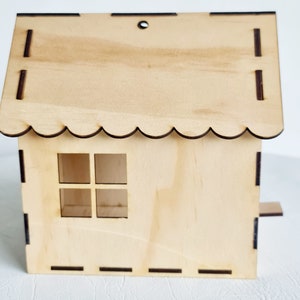 May include: A wooden birdhouse with a scalloped roof, a small window, and a perch. The birdhouse is made of light brown wood and has a natural finish.