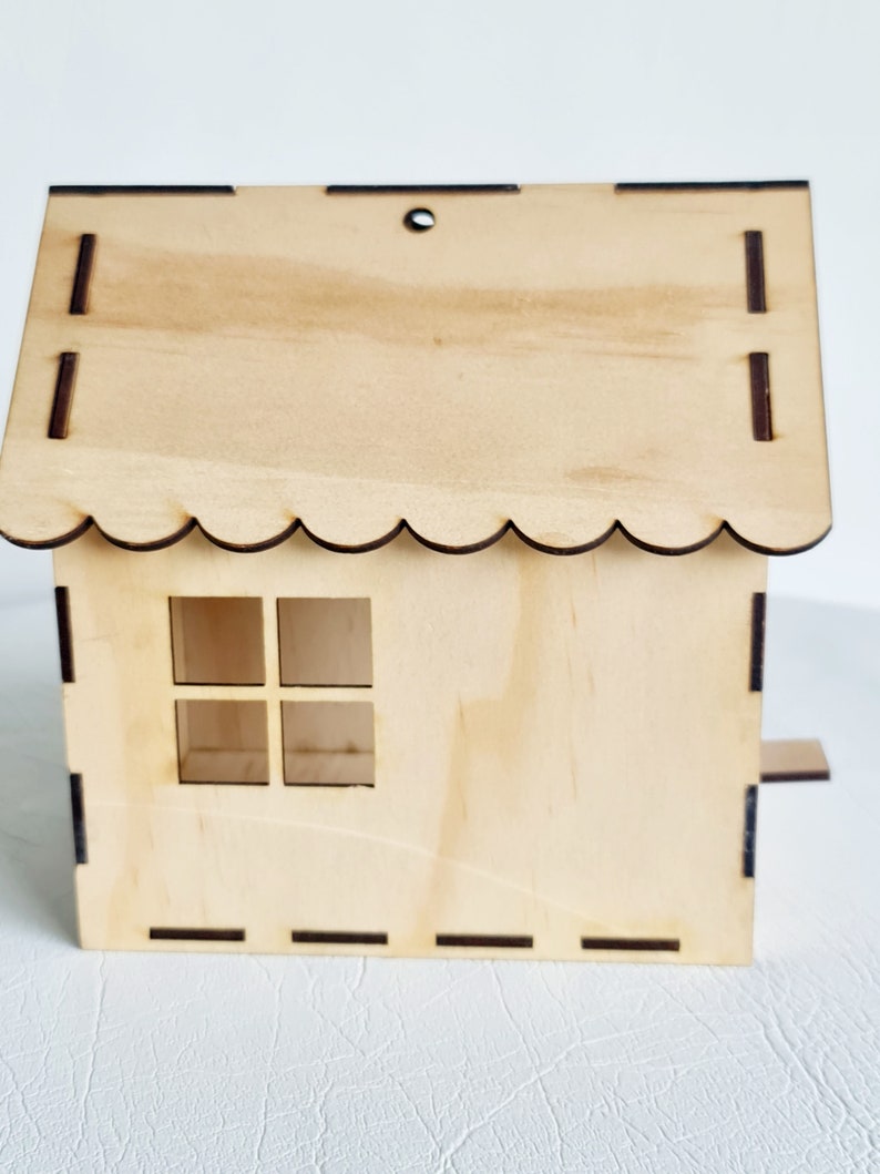 May include: A wooden birdhouse with a scalloped roof, a small window, and a perch. The birdhouse is made of light brown wood and has a natural finish.