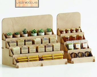 May include: Wooden display stands with multiple tiers, displaying a range of items. The stands feature small potted succulents, wrapped soaps, jars of honey, small bags of herbs, and candles. The sign at the top reads "LASER WOOD LAB".