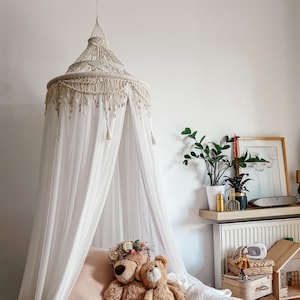 Peut inclure: Un lit à baldaquin blanc avec une couverture de lit marron et deux ours en peluche. Le lit est décoré d'une couronne de fleurs et d'une couverture blanche.