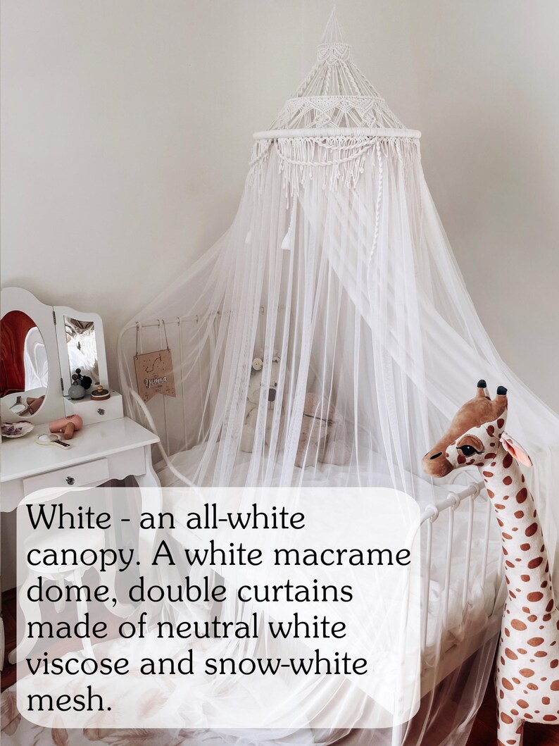 May include: White macrame canopy with a white dome and double curtains made of neutral white viscose and snow-white mesh. The canopy is hanging over a white bed with a stuffed giraffe toy.