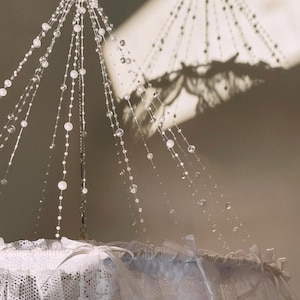 May include: A white lace canopy with a beaded chandelier hanging from the centre. The beads are clear and reflect light.